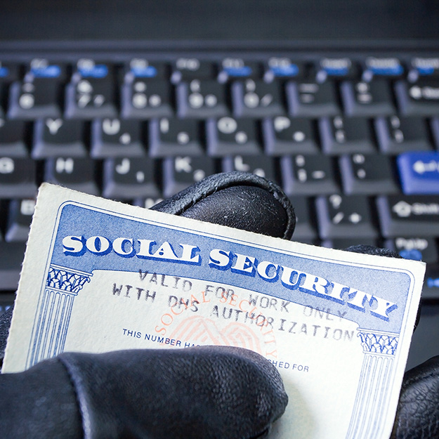 Gloved hand holding Social Security card in front of keyboard